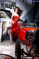 A woman in a red dress standing next to a red car.