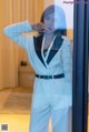 A woman in a white suit standing in front of a glass door.