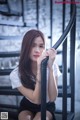 A woman sitting on a metal railing with her hand on her chin.