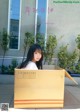 A woman sitting in a cardboard box in front of a building.