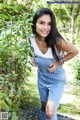 A woman in a white tank top and blue overalls posing for a picture.