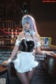 A woman dressed as a maid standing in front of a bar.