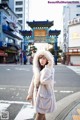 A woman in a white coat is standing in the middle of the street.