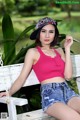 A woman in a pink top and denim shorts sitting on a bench.