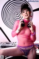 A woman in a pink top and fishnet stockings holding a pair of headphones.