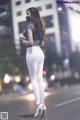 A woman wearing white pants and a face mask standing on the street.