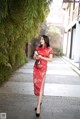 A woman in a red cheongsam standing on a sidewalk.