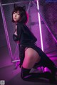 A woman in a black cat suit posing in front of a neon sign.
